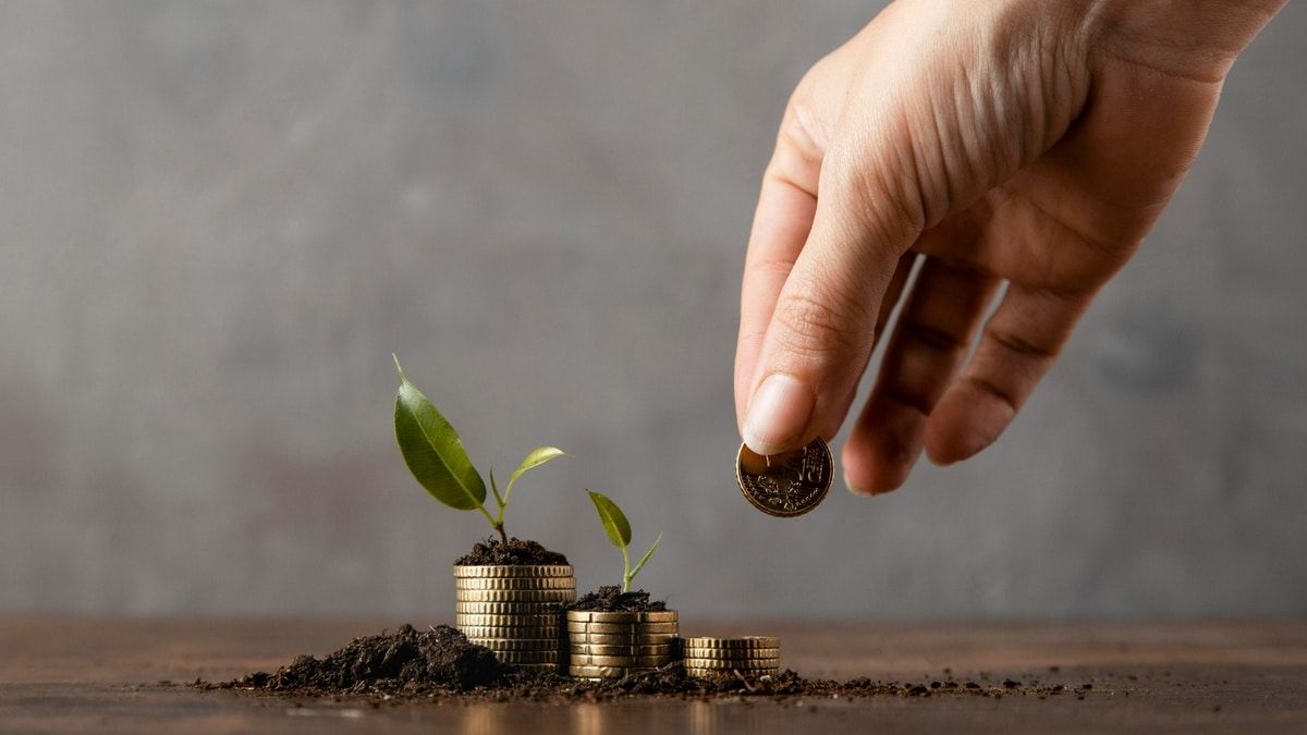 Una mano humana coloca una moneda dorada sobre una pila de monedas cubiertas de tierra, de las cuales brotan pequeñas plantas verdes, simbolizando el crecimiento financiero y la inversión sostenible.